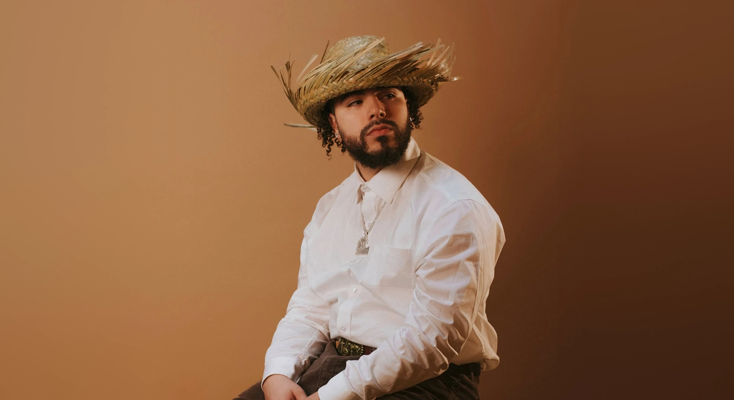 Kenny Rivers in a straw hat and white shirt against a warm studio backdrop